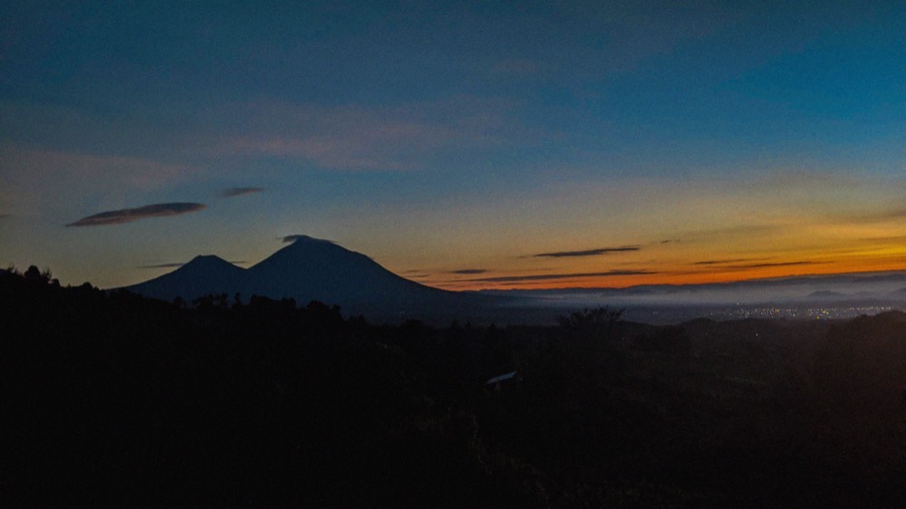 The Muhabura and Gahinga volcanoes rising above green farmland at sunrise near Volcanoes National Park, Rwanda.